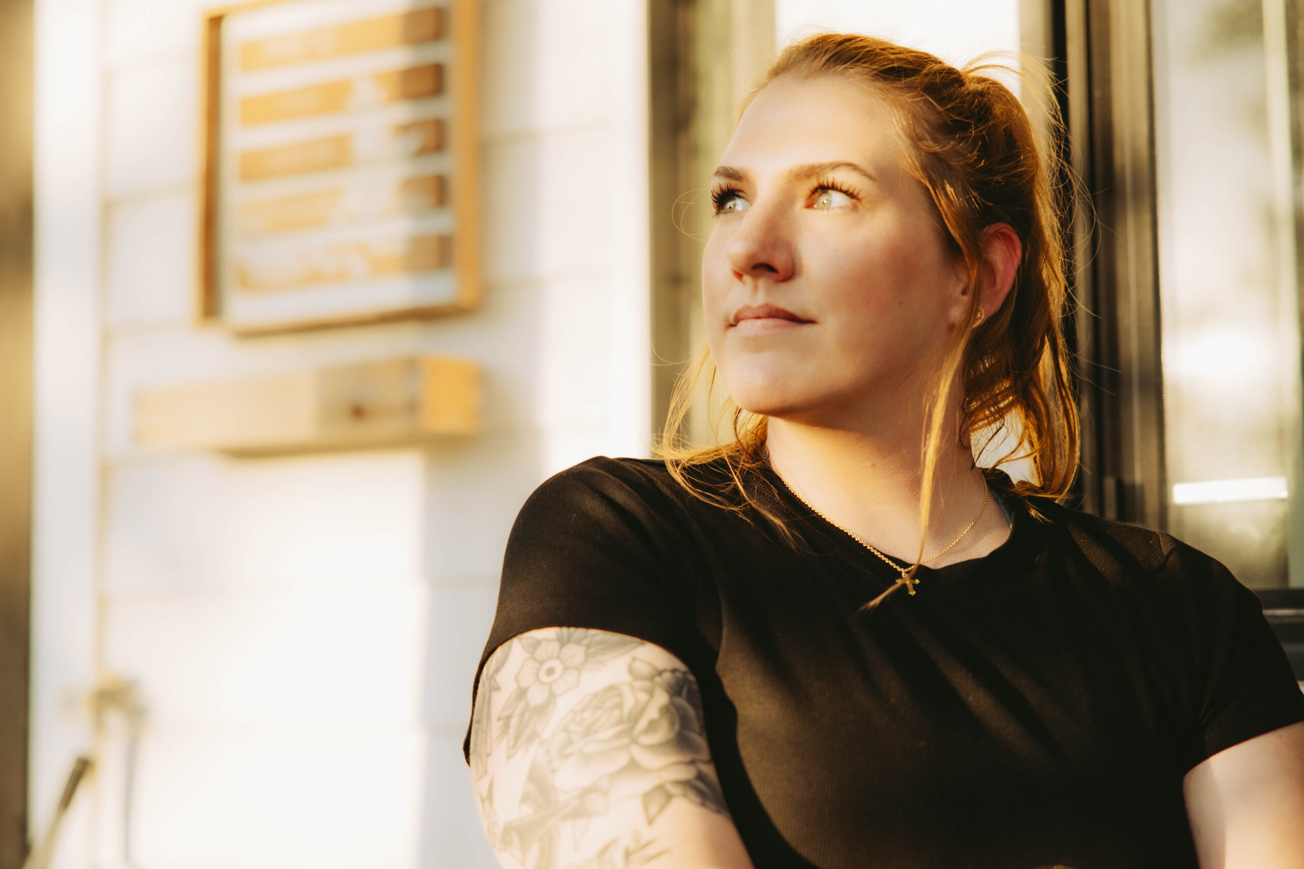 Caiti Loomis, wedding and portrait photographer at Caiti Rose Photography, standing by a window